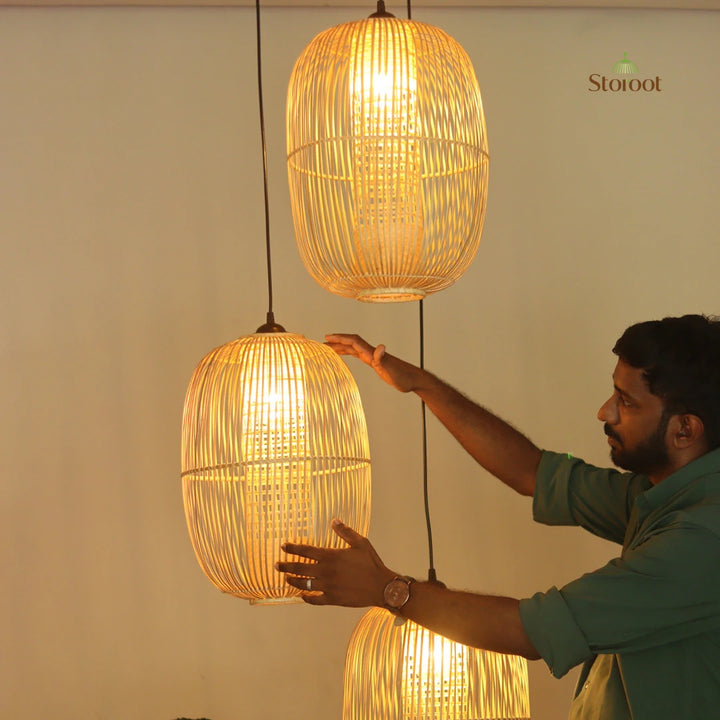 Three hanging woven rattan pendant lights in warm yellow glow, shown in a room setting with a man adjusting the middle light. The Staroot brand logo is visible in the top right corner.